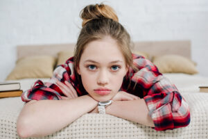 A photo of a teen girl laying on her bed and dreading going back to school