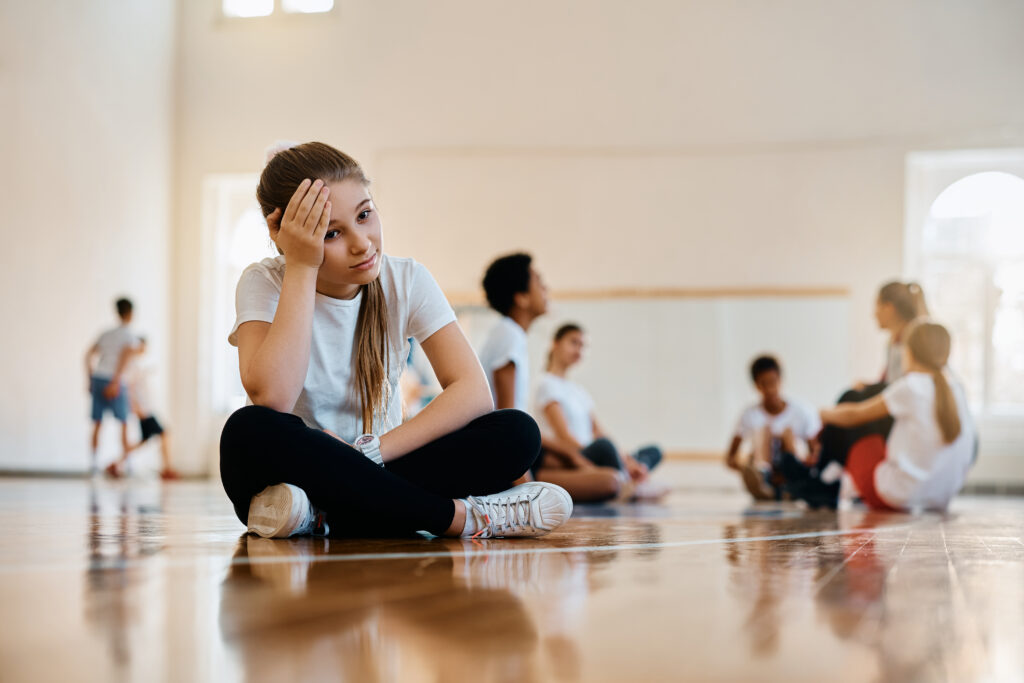 A photo of a stressed out teenage sitting in a gym and struggling with balancing school sports and academics
