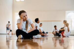 A photo of a stressed out teenage sitting in a gym and struggling with balancing school sports and academics